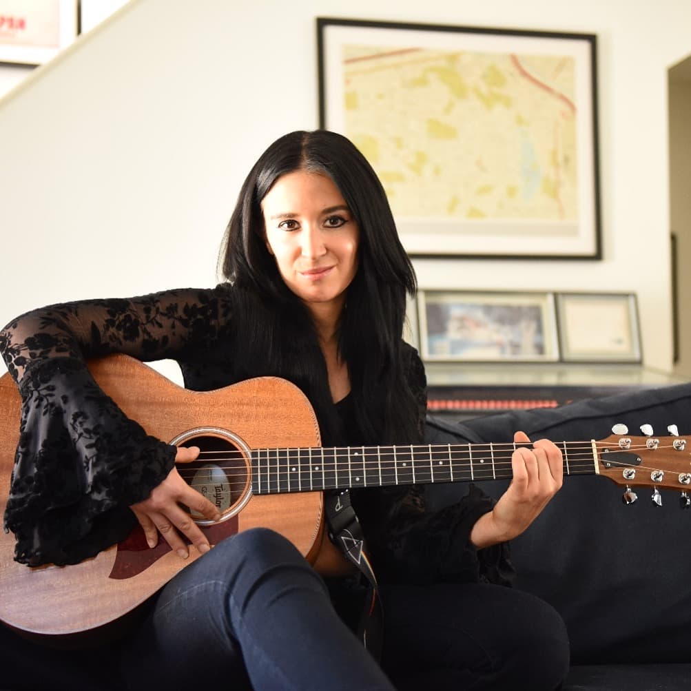 Jackie holding a Taylor acoustic guitar — the small-format intimate band variant.