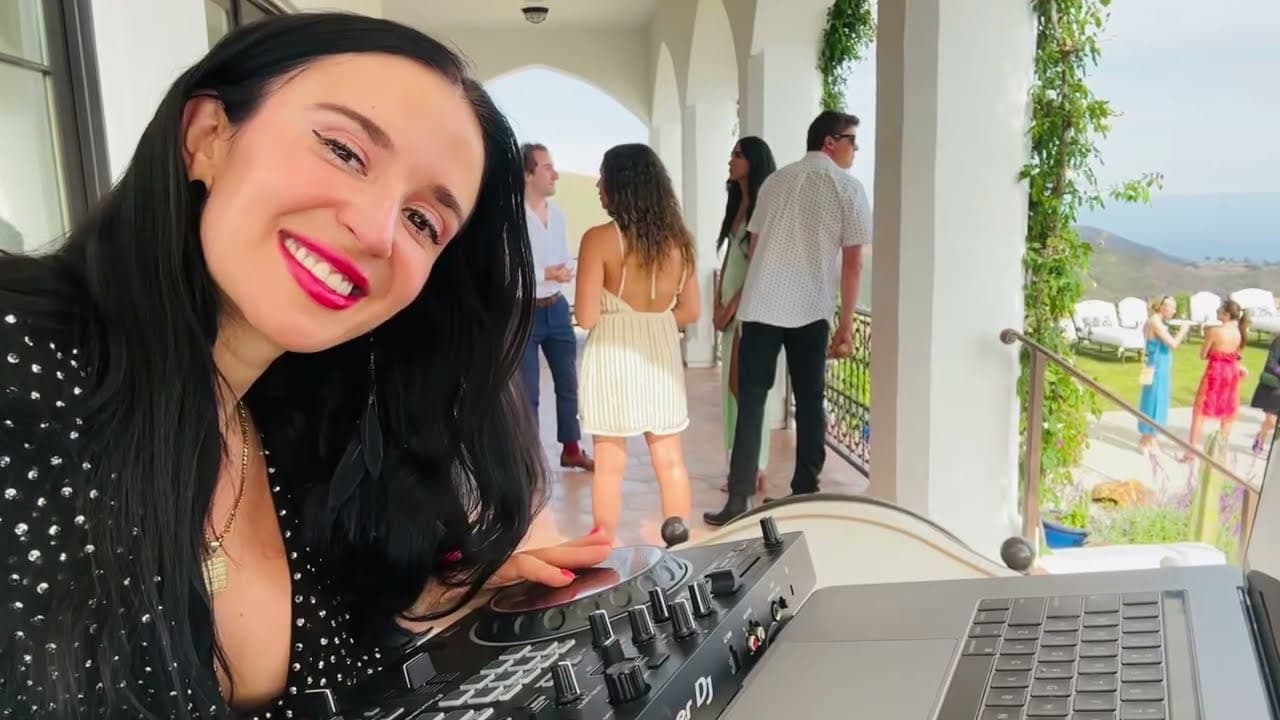 Close-up of Jackie smiling behind her Pioneer DJ rig on a cliffside Malibu terrace.